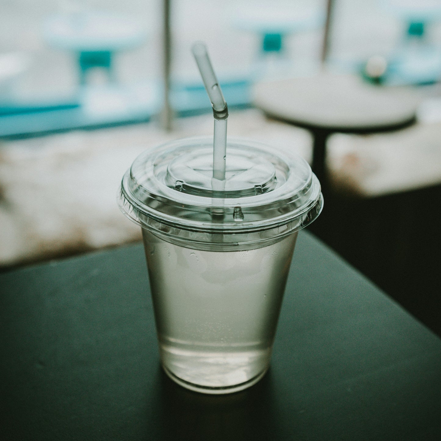 Clear plastic cup with a straw on a dark surface, blurred background