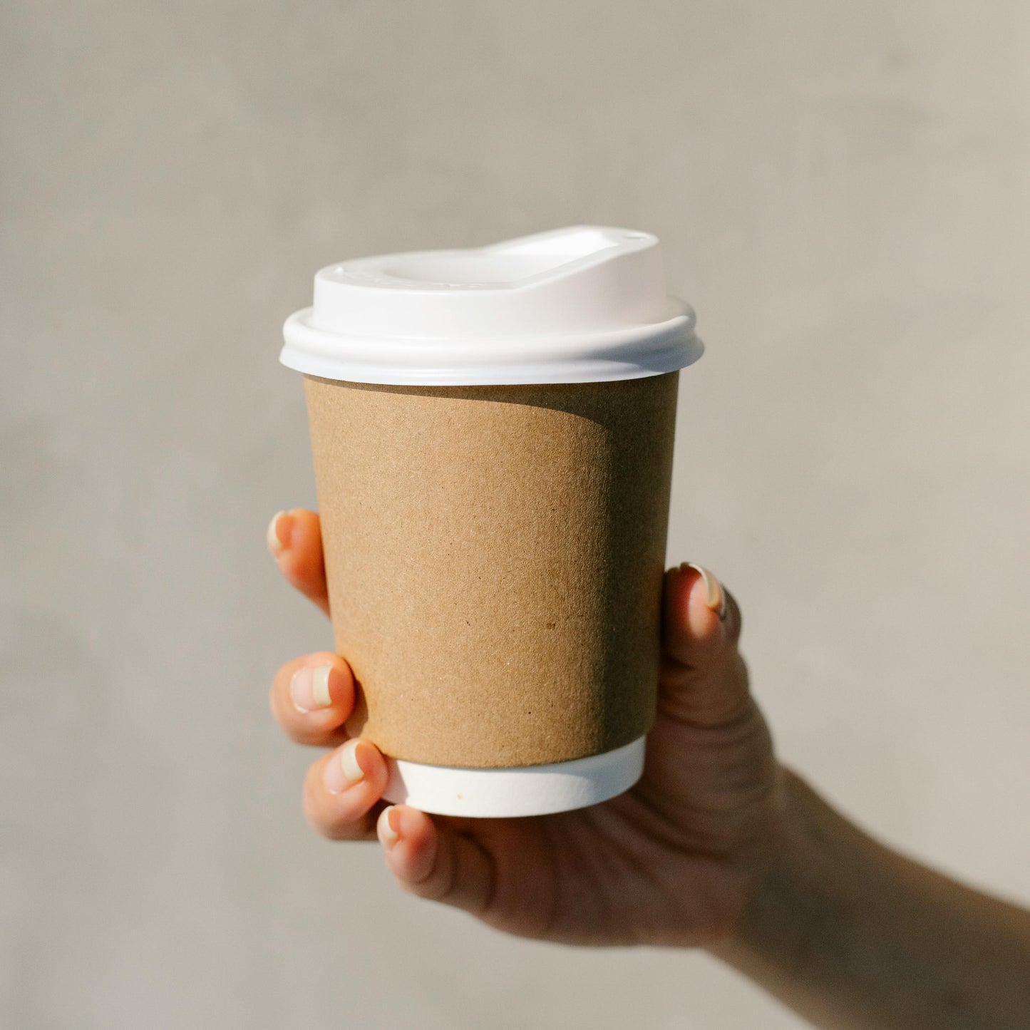 Hand holding a paper coffee cup with a white lid against a neutral background